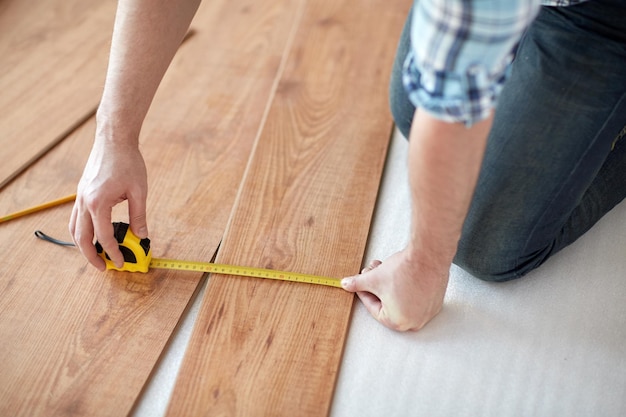 concept de réparation, de construction, de sol et de personnes - gros plan sur des mains masculines mesurant un sol en bois avec une règle et faisant une marque au crayon