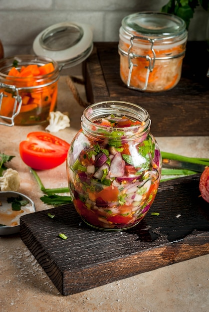 Photo concept d'un repas fermenté. accueil en conserve et billettes. nourriture végétalienne. des légumes. boîtes de salsa en conserve, choucroute, carottes marinées, kimchi et brocoli de chou-fleur. table de cuisine à domicile. fond