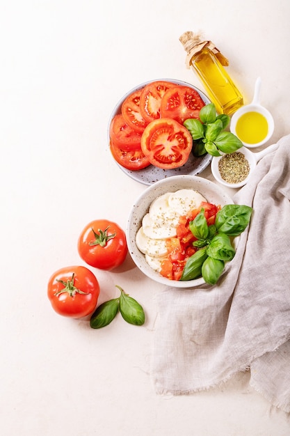 Concept de repas santé fait maison: tomates cerises, boules de mozzarella, épices, huile d'olive et basilic frais. Salade de mozzarella sur une surface de texture blanche. Vue de dessus, pose à plat