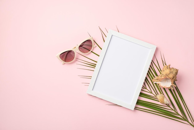 Concept de repos d'été Photo vue de dessus du cadre photo blanc lunettes de soleil à la mode coquilles et feuilles de palmier sur fond rose pastel isolé avec espace pour copie