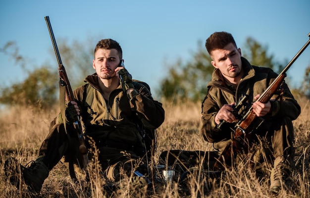 Concept de repos pour les vrais hommes Les chasseurs avec des fusils se détendent dans l'environnement naturel La chasse avec des amis passe-temps Les chasseurs sont satisfaits de la boisson réchauffante Les amis des chasseurs apprécient les loisirs