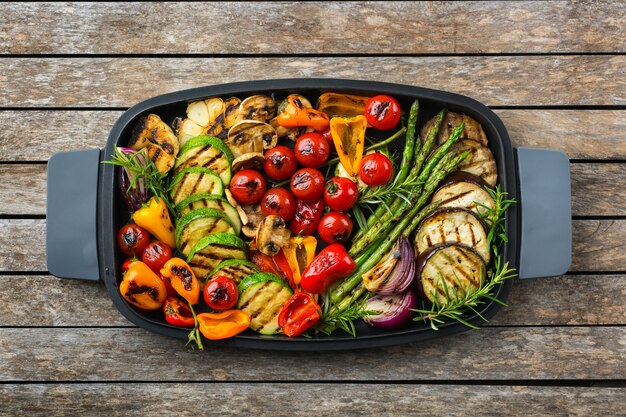 Concept de restauration végétalienne, végétarienne, saisonnière et estivale. Légumes grillés dans une casserole sur une table en bois. Vue de dessus fond plat