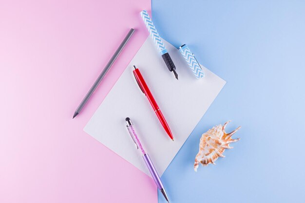 Concept de retour à l'école Articles de papeterie scolaire et coquillages sur fond rose-bleu Plumes multicolores