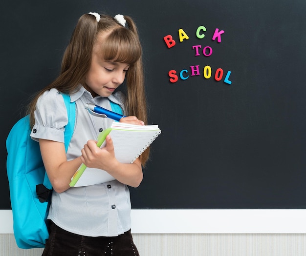 Concept de retour à l'école Écolière heureuse avec sac à dos et cahier au tableau noir en classe