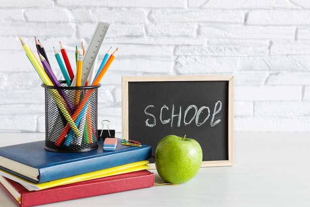 Concept de retour à l'école avec des livres, des crayons colorés et une pomme sur une table en bois blanche