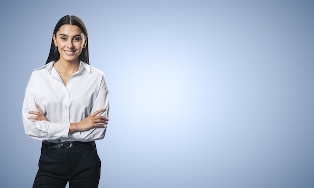 Concept de réussite commerciale avec une jeune femme d'affaires souriante, pliant ses mains en chemise blanche et pantalon noir sur fond blanc abstrait bleu clair avec place pour votre logo ou texte Maquette