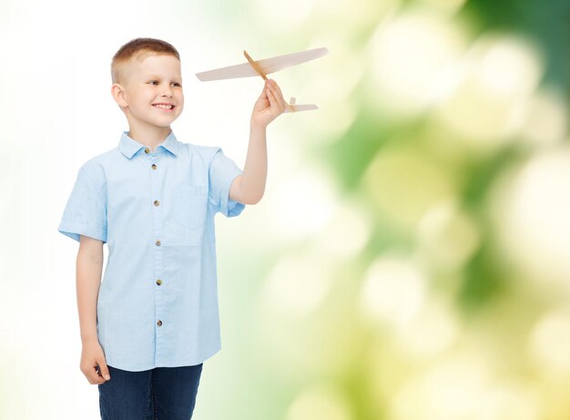 concept de rêves, d'avenir, de passe-temps, d'écologie et d'enfance - petit garçon souriant tenant un modèle d'avion en bois dans sa main sur fond vert