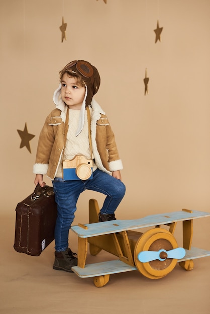 concept de rêves et de voyages. pilote aviateur enfant avec un jouet avion et valise joue dans un beige