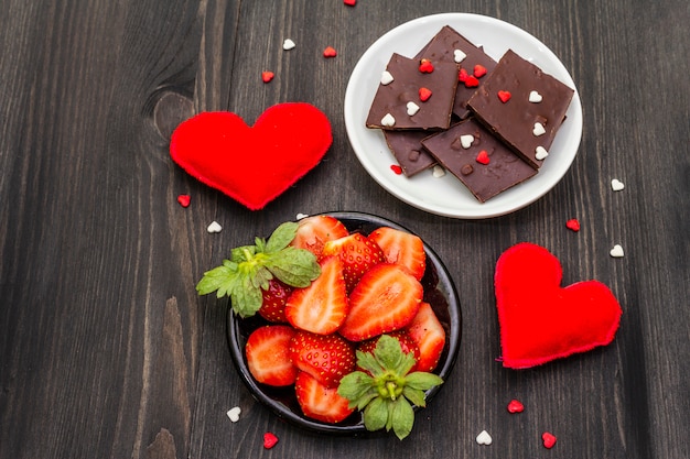 Concept romantique de la Saint-Valentin. Chocolat, fraise mûre fraîche, coeurs en feutre rouge. Dessert sucré pour les amoureux.