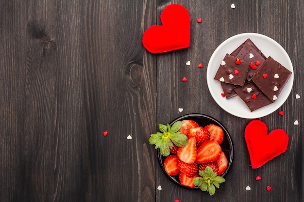 Concept romantique de la Saint-Valentin. Chocolat, fraise mûre fraîche, coeurs en feutre rouge. Dessert sucré pour les amoureux.