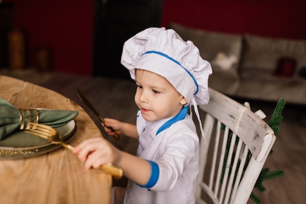 Concept de saine alimentation. Heureux petit garçon cuisine dans la cuisine par une journée d'été ensoleillée. Tout-petit boulanger sur un pique-nique mange du pain et des bagels dans un tablier blanc et un chapeau