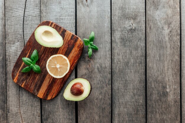 Concept de saine alimentation à plat. Régime méditerranéen, planche à découper avec moitiés d'avocat, noyau, grappes de basilic et moitié citron sur table en bois. La nourriture végétarienne. Concept de nourriture saine. Alimentation biologique