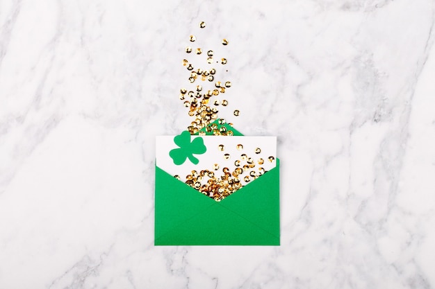 Concept de la Saint-Patrick. Carte vide avec enveloppe verte et confett doré et feuille de trèfle. Modèle de maquette. Vue d'en-haut