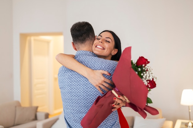 Concept de la Saint-Valentin. Les amoureux s'embrassent. Bel homme surprend sa petite amie avec des roses rouges à la maison