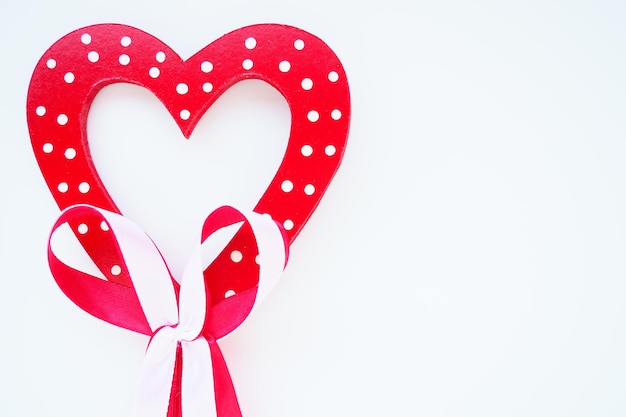 Concept de la Saint-Valentin. Coeur en bois rouge à pois blancs et noeud de ruban sur un bâton. Fond blanc. Un bel arc comme décoration. Amour et relations. Reconnaissance ou félicitations