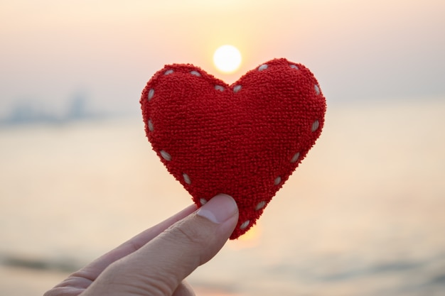 Concept de Saint Valentin, concept de l&#39;amour, main de femme tenant un coeur rouge sur fond de coucher de soleil.