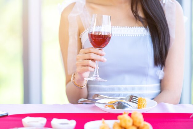 Concept de la Saint-Valentin, jeune fille asiatique assise à une table avec des verres à vin et un bouquet de vin de roses rouges et roses et attendant son homme à l'arrière-plan du restaurant