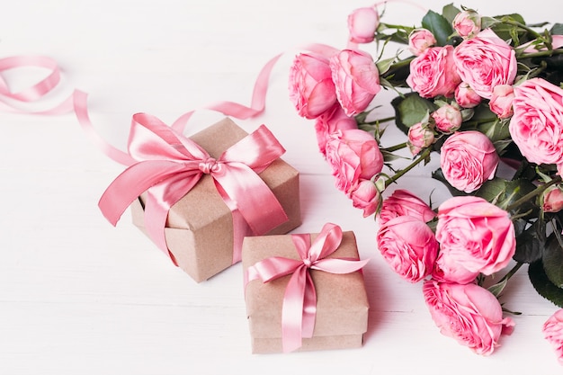 Concept de la Saint-Valentin. Roses roses et coffrets cadeaux avec des rubans sur une table en bois blanche.