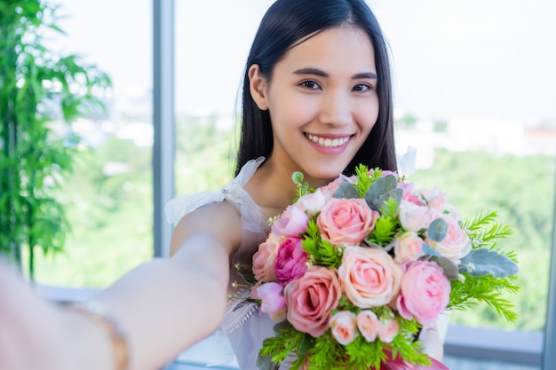 Concept de la Saint-Valentin, Selfie of Happy of smiling Asian young female sitting at a table food holding a bouquet of roses at in the restaurant