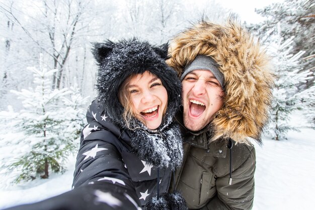 Concept de saison, d'amour, de technologie et de loisirs - couple heureux prenant selfie par smartphone pendant l'hiver