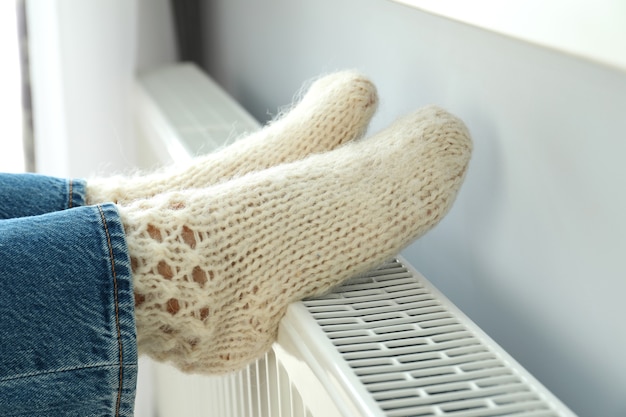 Concept de saison de chauffage avec jambes en bottes tricotées sur radiateur.