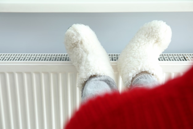 Photo concept de saison de chauffage avec jambes en bottes tricotées sur radiateur.