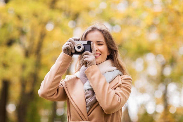 concept de saison, de photographie et de personnes - belle jeune femme heureuse prenant une photo avec un appareil photo vintage dans le parc d'automne