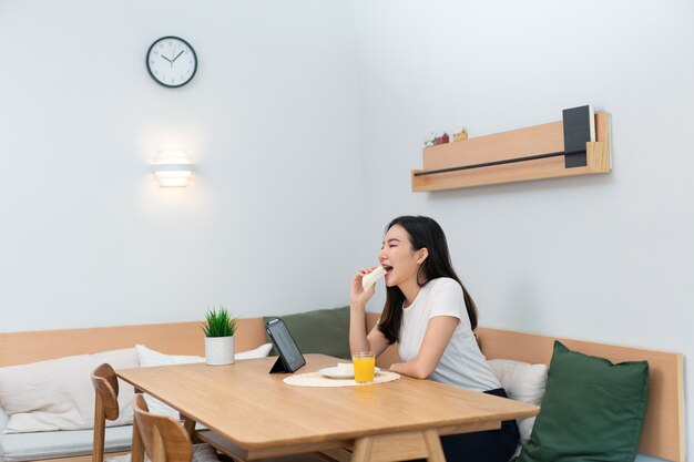 Concept de salon une femme adulte appréciant de manger des sandwichs et du jus d'orange en regardant les médias en ligne pendant la pause de travail.