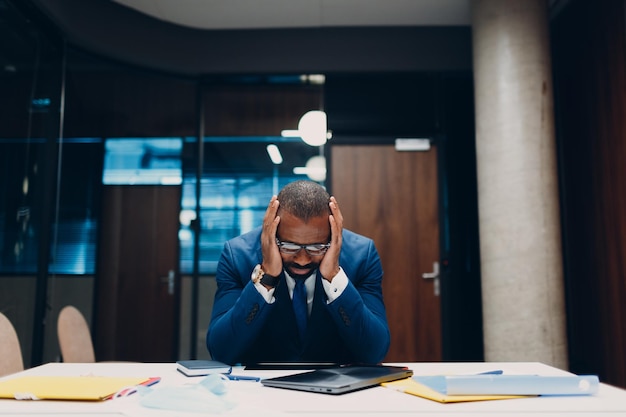 Concept sanctions économiques crise financière et faillite Triste homme d'affaires noir afro-américain s'asseoir et tenir la tête avec ses mains à la table de bureau