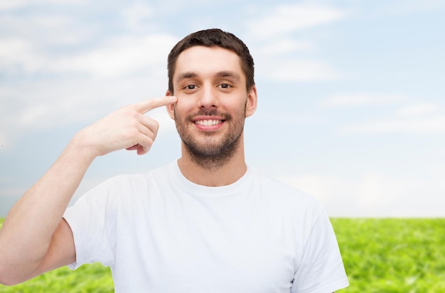 concept de santé et de beauté - souriant jeune bel homme pointant vers les yeux