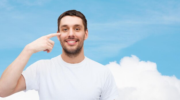 concept de santé et de beauté - souriant jeune bel homme pointant vers les yeux