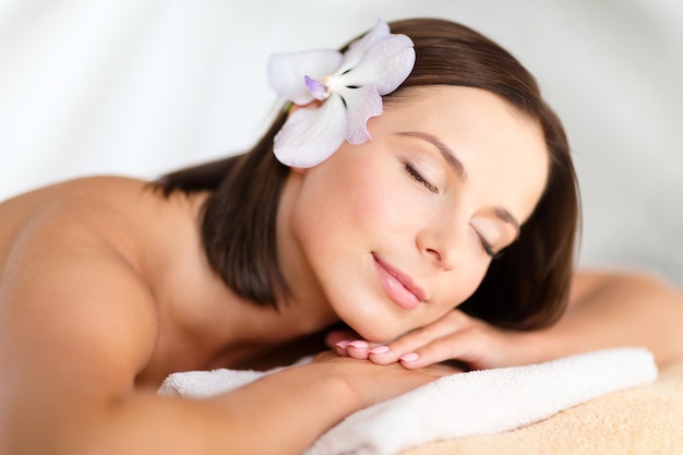 concept de santé et de beauté, de villégiature et de détente - belle femme avec une fleur dans les cheveux dans un salon de spa allongé sur le bureau de massage