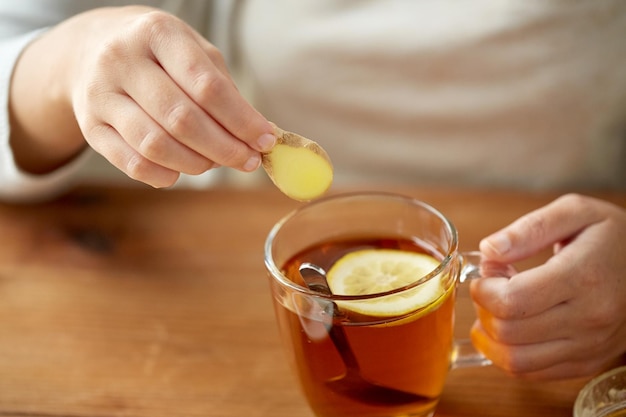 concept de santé, de médecine traditionnelle et d'ethnoscience - gros plan d'une femme ajoutant du gingembre à une tasse de thé au citron