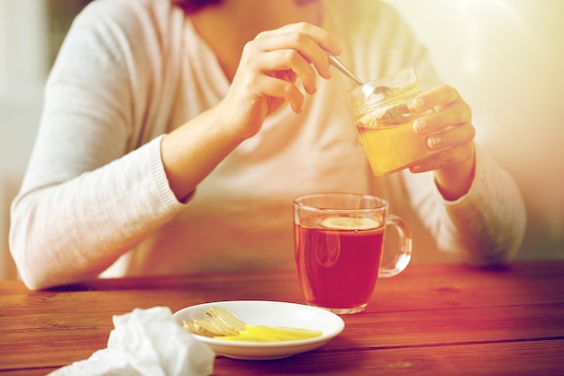 concept de santé, de médecine traditionnelle et d'ethnoscience - gros plan d'une femme ajoutant du miel au thé au citron