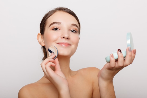 Concept de santé, de personnes et de beauté - Jeune femme appliquant un fard à joues sur son visage avec une houppette, concept de soins de la peau, composition photo d'une fille brune, isolée sur fond blanc