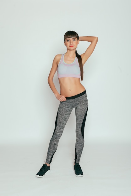 Concept de santé, de personnes, de sport et de style de vie - Jeune fille heureuse de remise en forme avec un corps sportif au studio sur une surface grise