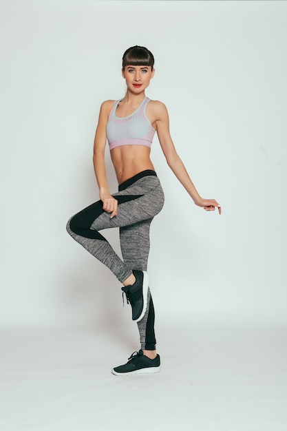 Concept de santé, de personnes, de sport et de style de vie - Jeune fille heureuse de remise en forme avec un corps sportif en studio sur fond gris. Belle fille en forme. Modèle de remise en forme en vêtements de sport gris. Mode de vie sain.