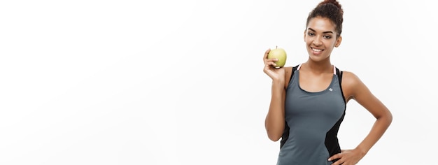 Concept de santé et de remise en forme Belle dame africaine américaine en vêtements de fitness gris tenant une pomme verte isolé sur fond blanc