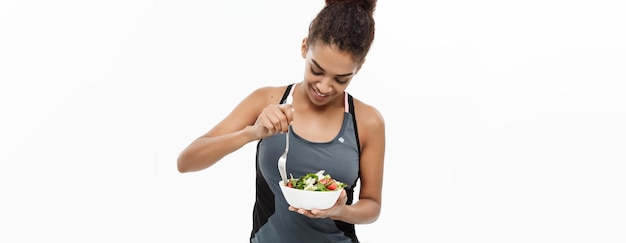 Concept de santé et de remise en forme Belle dame africaine américaine en vêtements de fitness sur le régime alimentaire manger de la salade fraîche isolé sur fond blanc