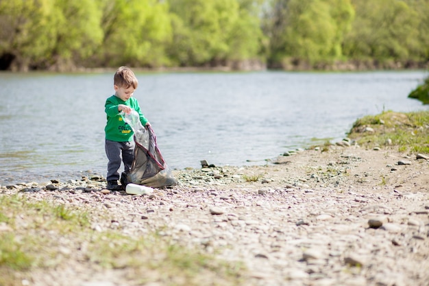 Photo concept de sauvegarde de l'environnement, un petit garçon ramassant des ordures et des bouteilles en plastique sur la plage pour les jeter à la poubelle.