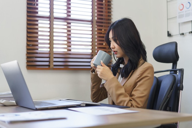 Concept de secrétaire Femme secrétaire buvant du café pendant la lecture du rapport d'activité sur un ordinateur portable