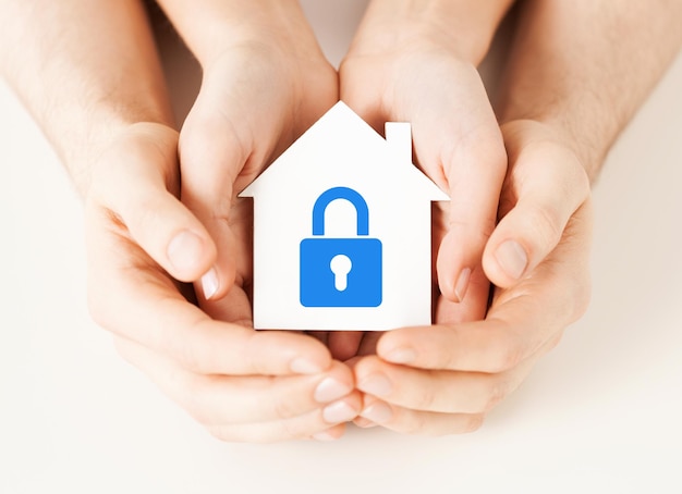 Photo concept de sécurité de l'immobilier et de la maison familiale - photo en gros plan de mains masculines et féminines tenant une maison en papier blanc avec serrure bleue