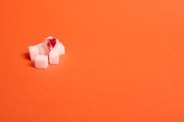 Concept de sensibilisation à la journée mondiale du diabète, 14 novembre. Cubes de sucre blanc pur et raffiné avec goutte de sang, isolés sur fond orange coloré avec espace de copie pour la publicité médicale