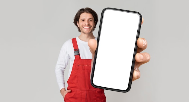 Concept de services de bricoleur souriant jeune ouvrier en uniforme montrant Smartphone