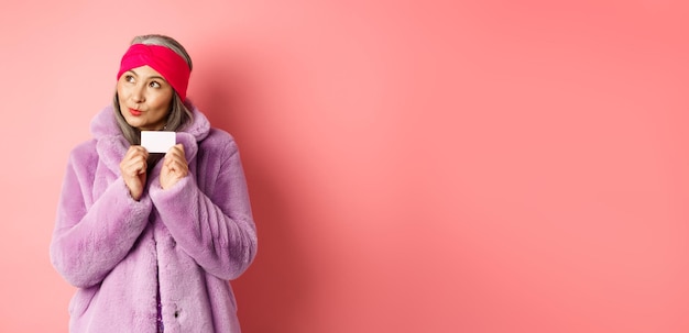 Photo concept de shopping et de mode femme senior asiatique à la mode pensant à acheter des cadeaux tenant la crédibilité