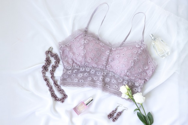 Concept de shopping et de mode. Soutien-gorge en dentelle lavande élégante femme, fleurs, bijoux, cosmétiques sur fond blanc. Pose à plat de lingerie élégante.