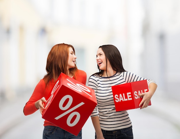 concept shopping, vente et cadeau - deux adolescentes souriantes avec un signe de pourcentage et de vente sur une boîte rouge dans la rue