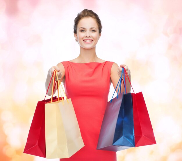 concept shopping, vente, noël et vacances - femme élégante souriante en robe rouge avec des sacs à provisions