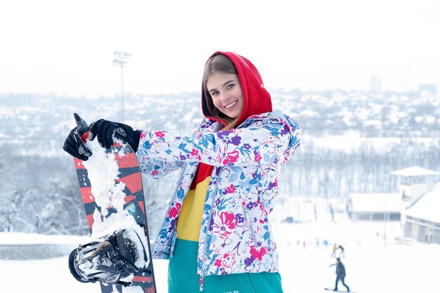 Photo concept de snowboard en plein air femme hiver. jeune femme tenant un snowboard sur ses épaules, elle regarde ailleurs et sourit, espace copie, gros plan