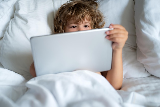 Concept social et technologique. Internet pour les enfants. Enfant avec tablette au lit. Autorisation parentale, réseau de sécurité en ligne. Garçon jouant à des jeux en ligne.